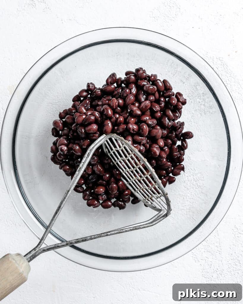 Hearty Vegan Black Bean and Bulgur Burgers 5 process shot of mashing beans in a glass bowl