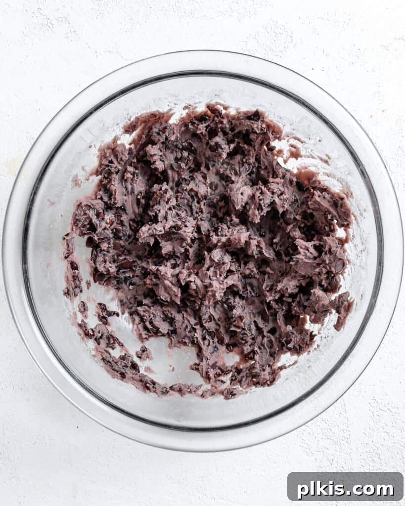 Hearty Vegan Black Bean and Bulgur Burgers 6 process shot of mashing beans in a glass bowl