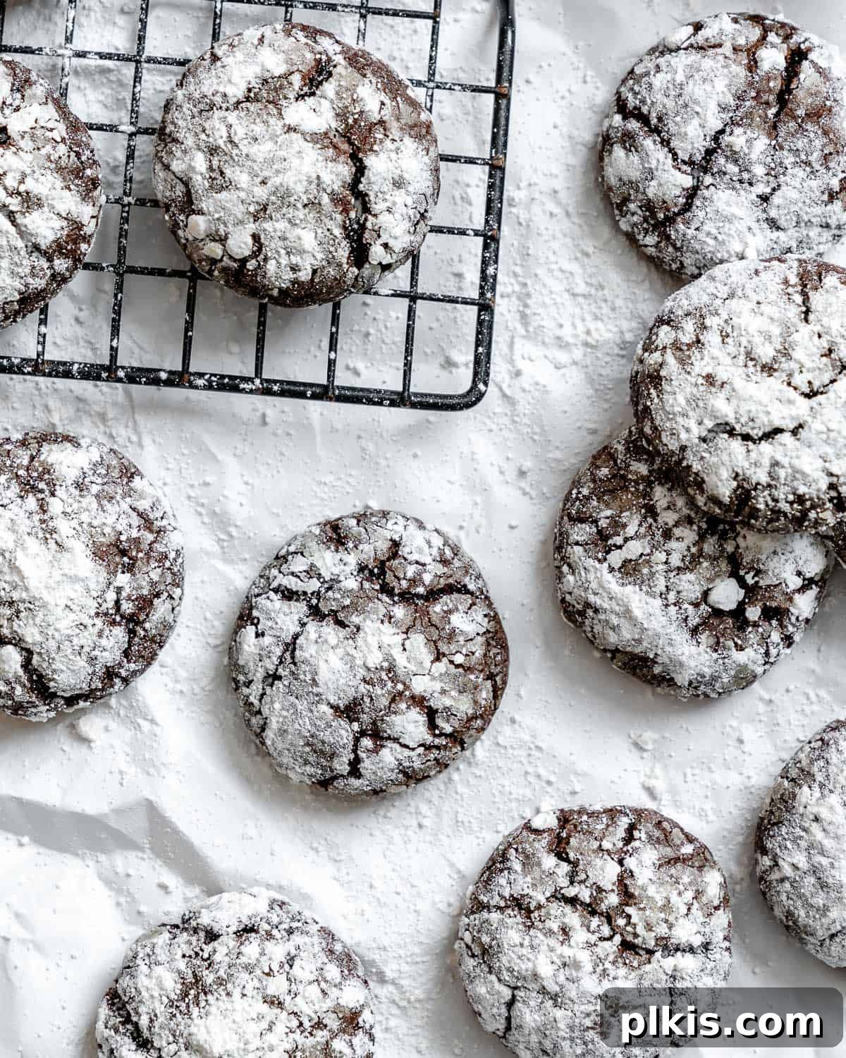 Completed Vegan Chocolate Crinkle Cookies on a white surface, showcasing their distinctive powdered sugar coating and crackled appearance.