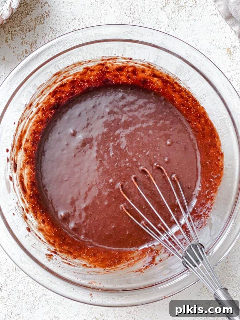 Process shot of mixing wet ingredients together in a large bowl, showing a whisk in action.