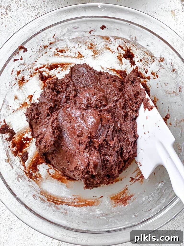 Process shot showing dry ingredients being mixed into wet ingredients in a bowl, forming the cookie dough.