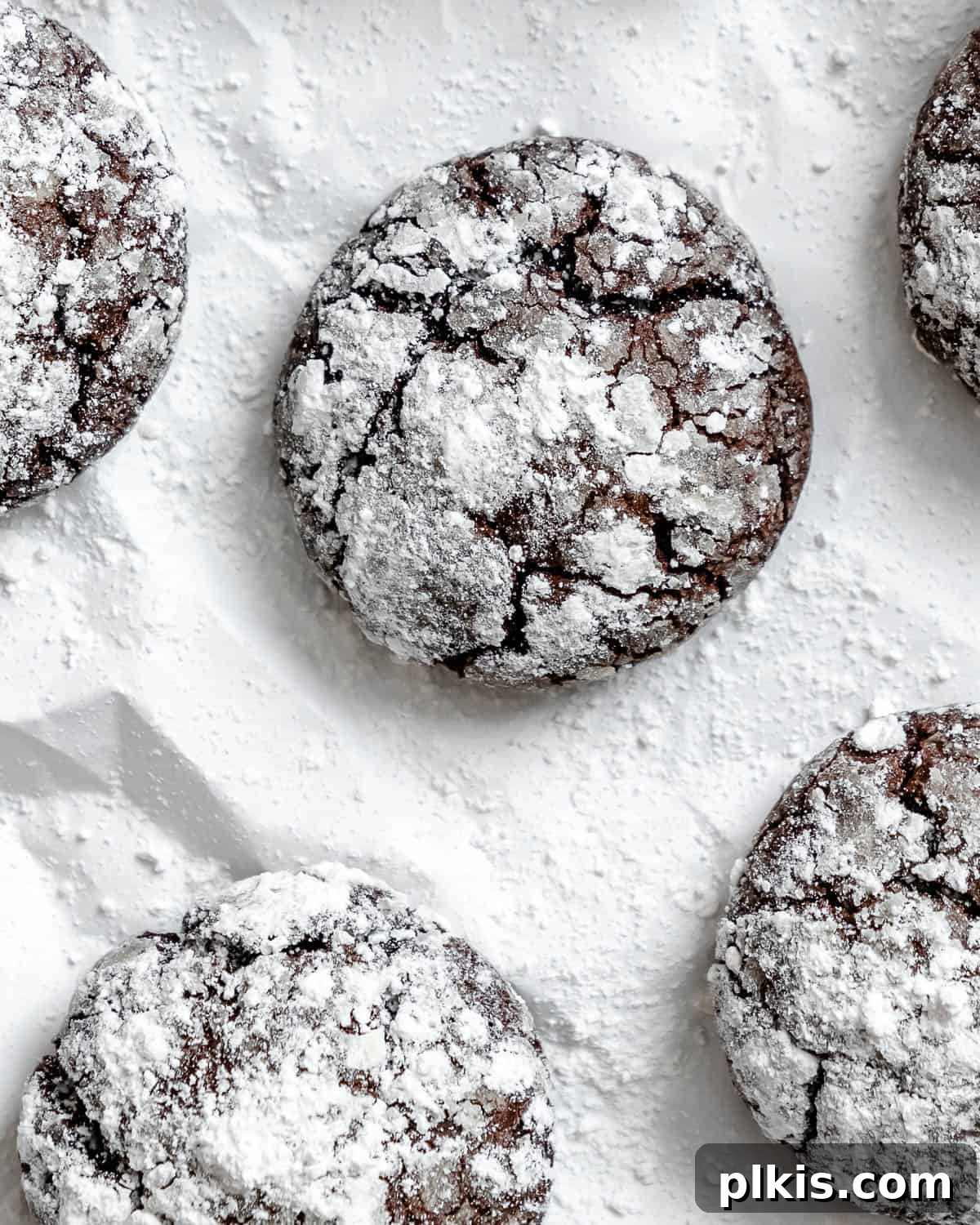 Completed Vegan Chocolate Crinkle Cookies arranged artfully on a white surface, highlighting their rich color and intricate cracks.