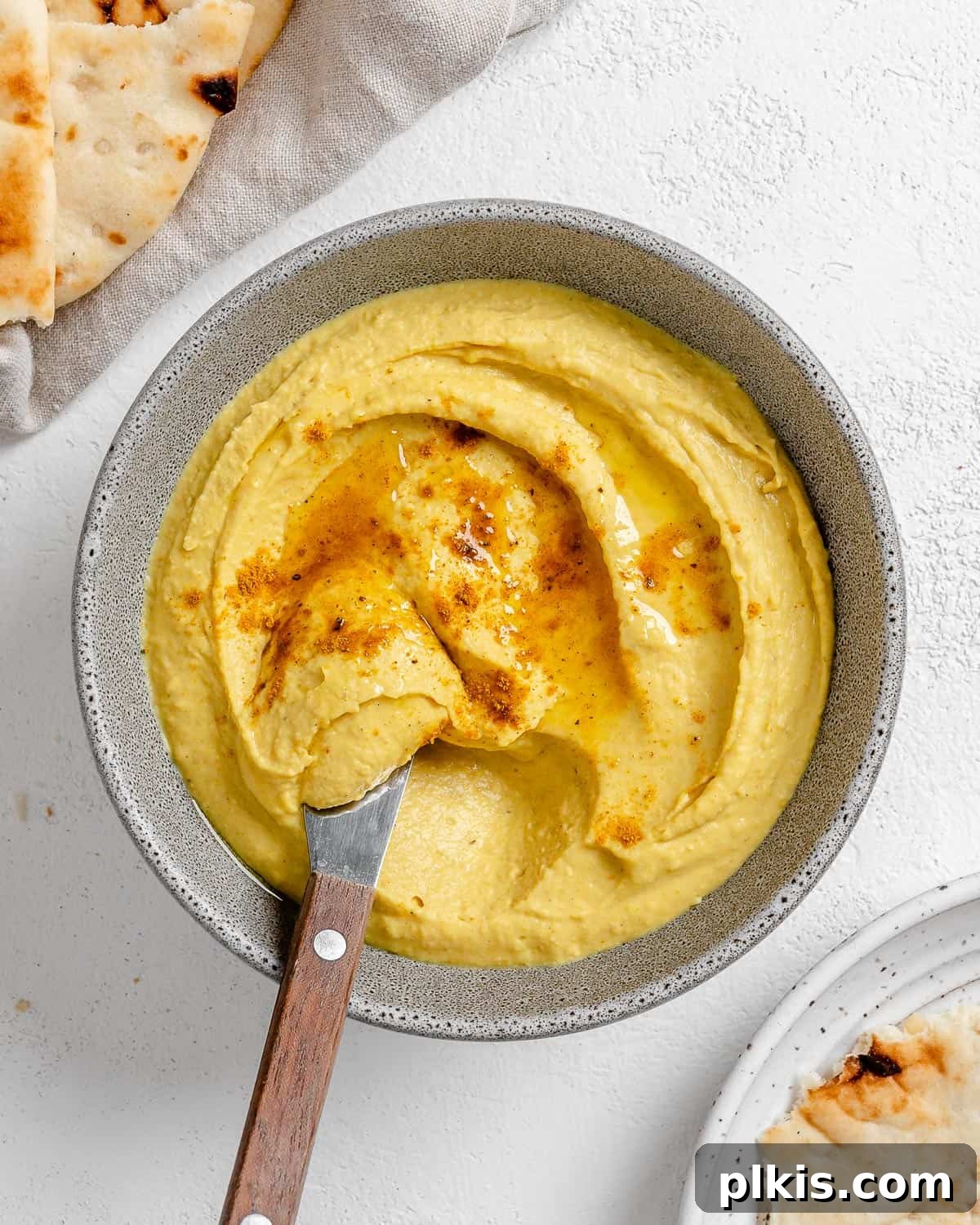 Creamy Vegan Curried White Bean Dip 2 Delicious Curried White Bean Dip served in a grey bowl with crusty bread for dipping, set against a white background.