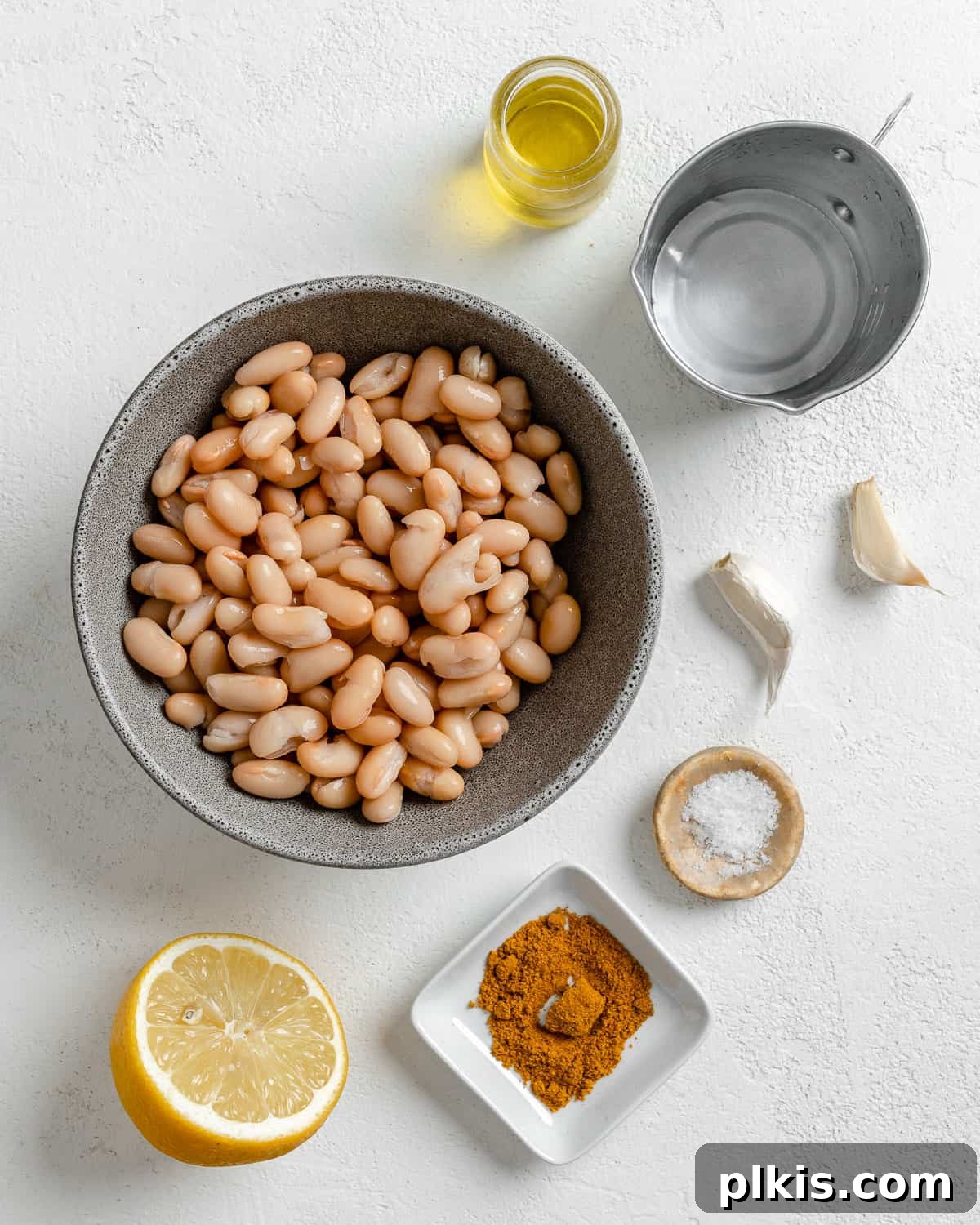 Creamy Vegan Curried White Bean Dip 3 All measured ingredients laid out for making curried white bean dip, including canned beans, lemon, olive oil, garlic, and curry powder, on a clean white surface.