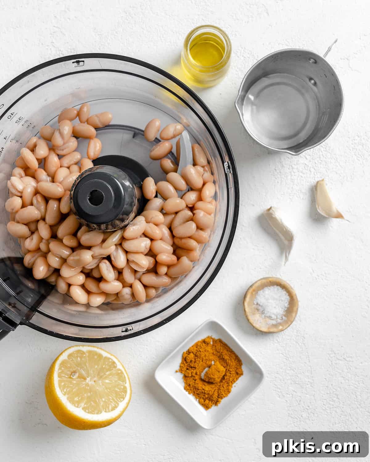 Creamy Vegan Curried White Bean Dip 4 Process shot showing ingredients being added to a food processor for curried white bean dip, with other ingredients waiting in the background.