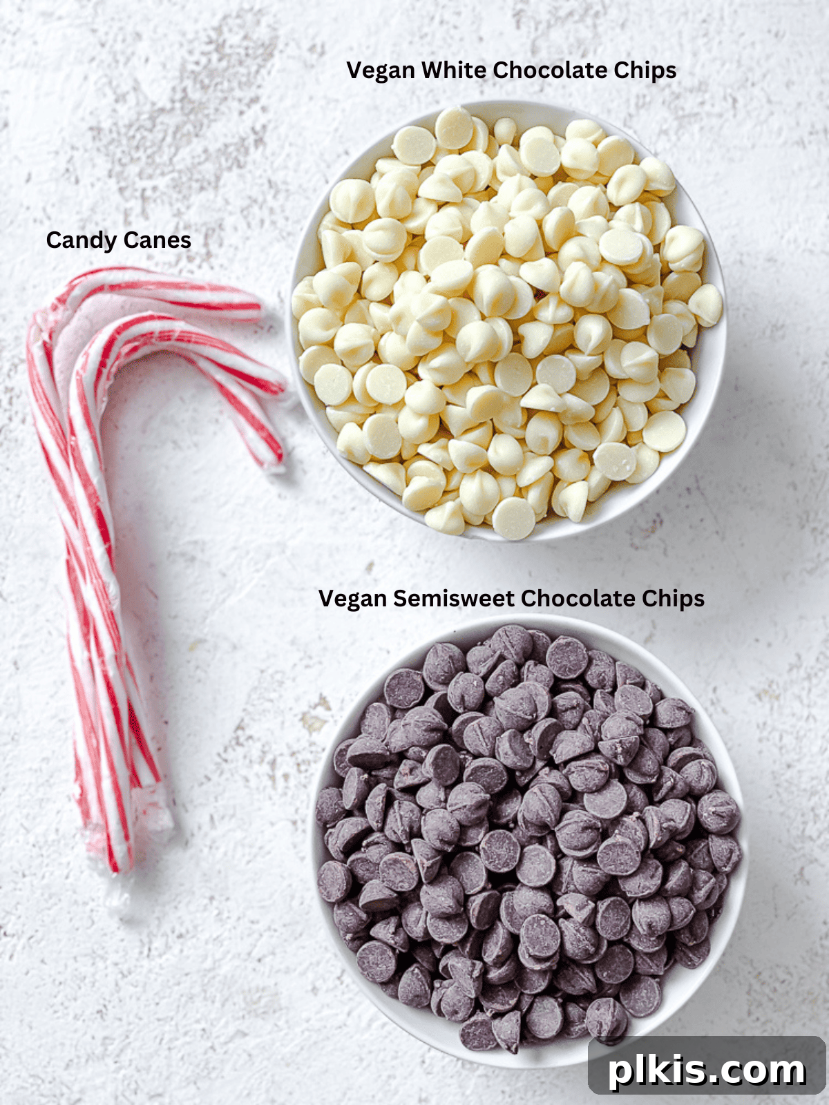 Ingredients for Vegan Peppermint Bark laid out on a white surface, including vegan chocolate chips, white chocolate chips, and candy canes.