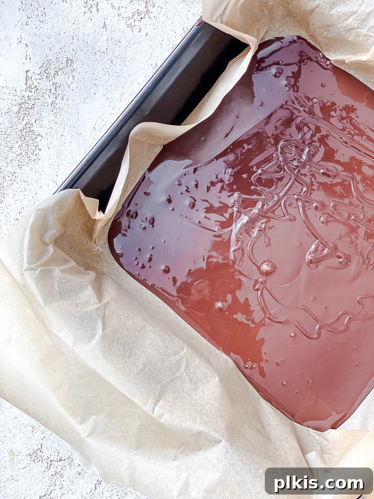 Process shot showing melted vegan dark chocolate poured into a parchment-lined baking dish.