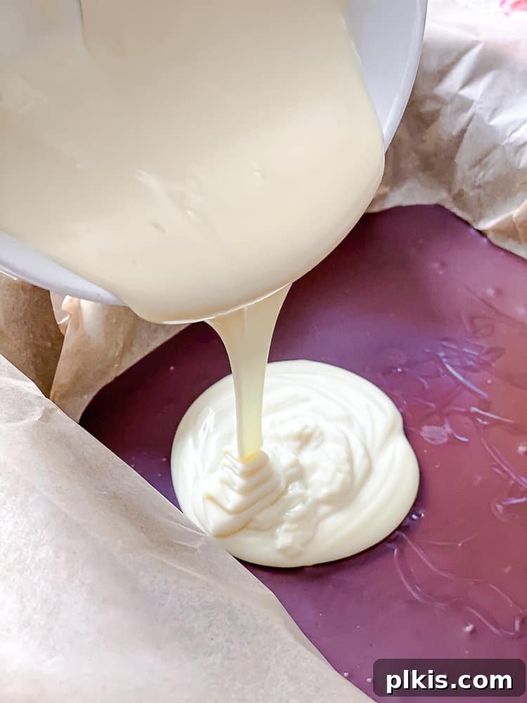 Process shot showing melted vegan white chocolate being carefully poured over the partially set dark chocolate layer in a baking dish.