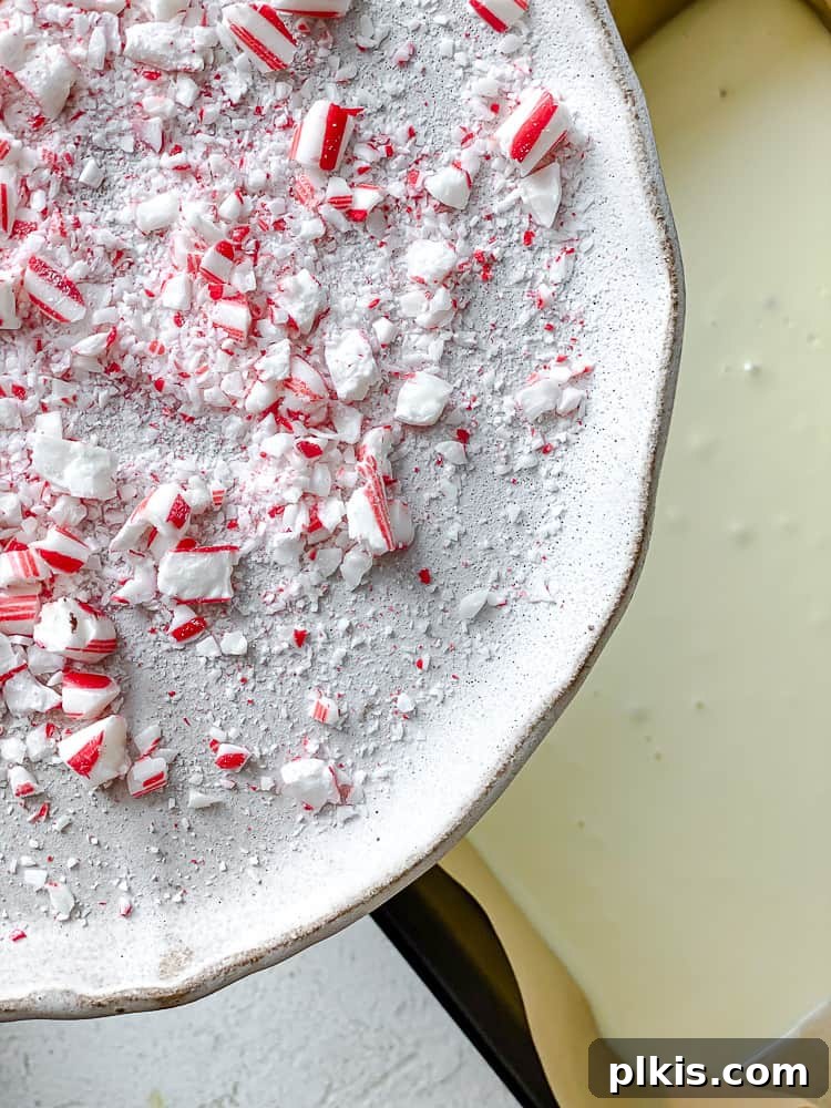 Process shot showing crushed peppermint candy being sprinkled over the two-layered vegan chocolate bark in a baking dish.