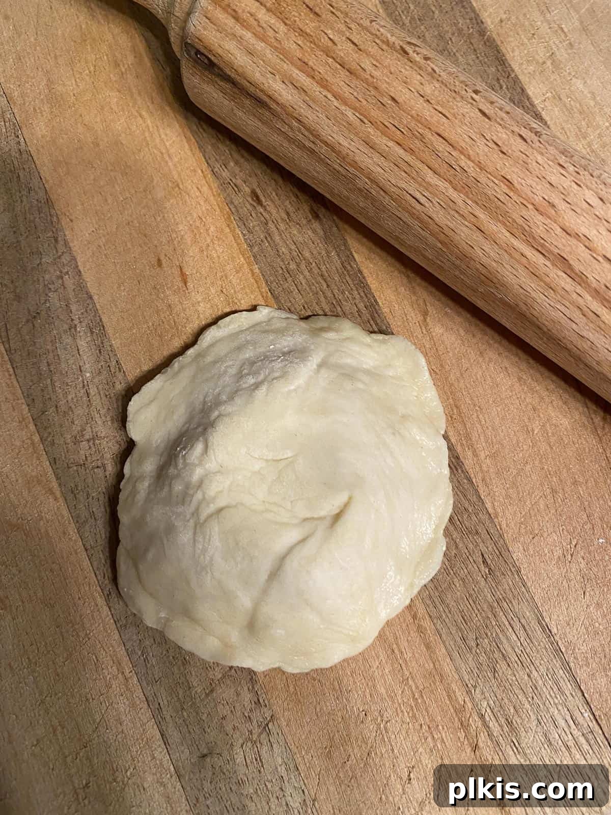 Delicate Chinese Wraps 13 A rolling pin flattening a double-layered dough circle into a thin, round pancake.