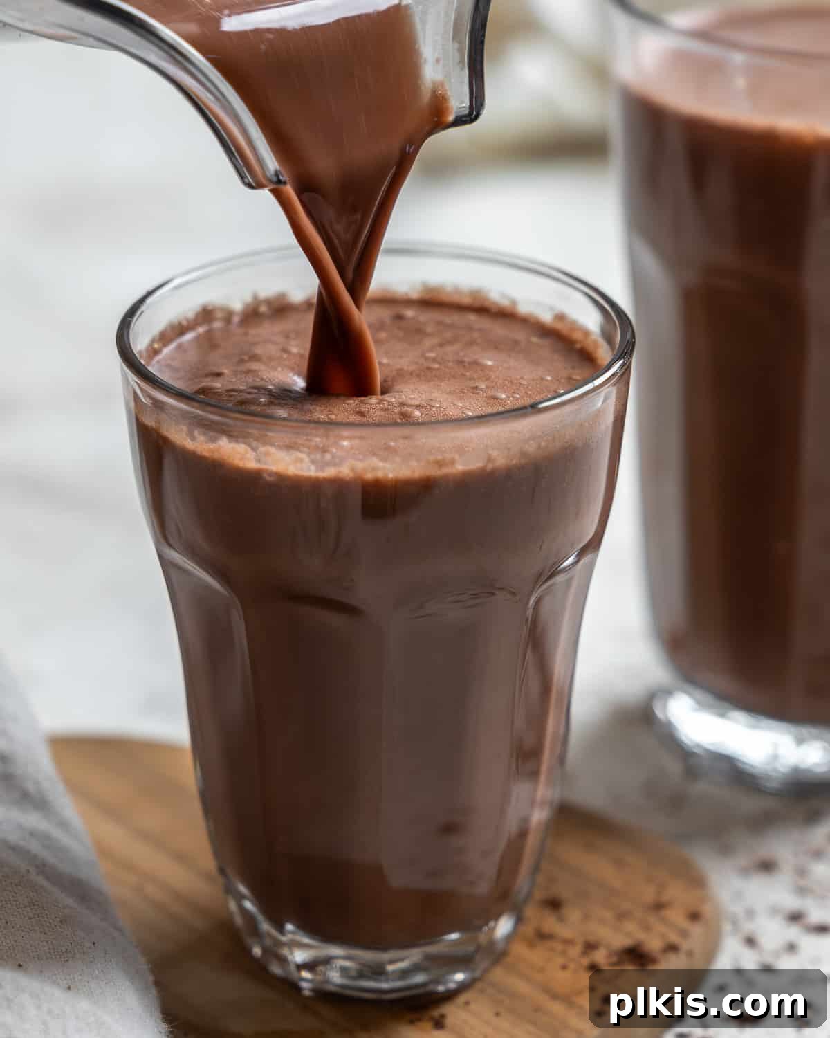 Homemade Chocolate Oat Milk being poured from a pitcher into a tall glass, showcasing its rich color and smooth texture.