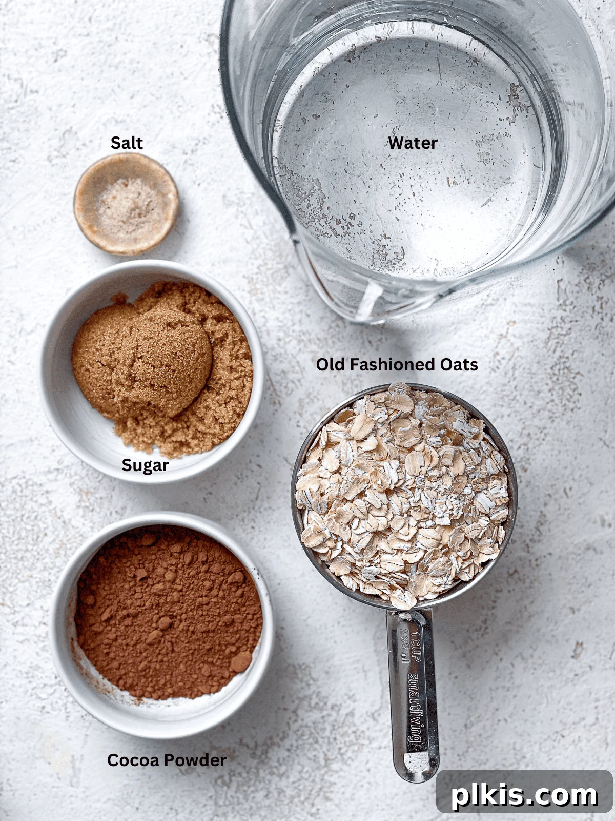 Array of ingredients for Chocolate Oat Milk laid out on a clean white surface, including oats, cocoa powder, sweetener, and salt.