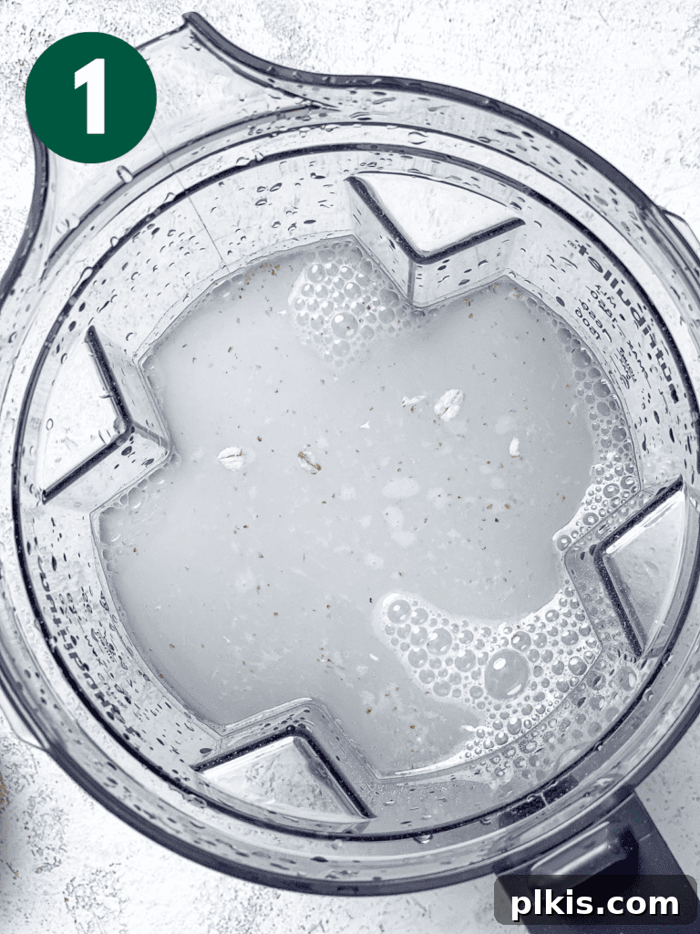 Process shot showing cold water and oats being added to a blender.