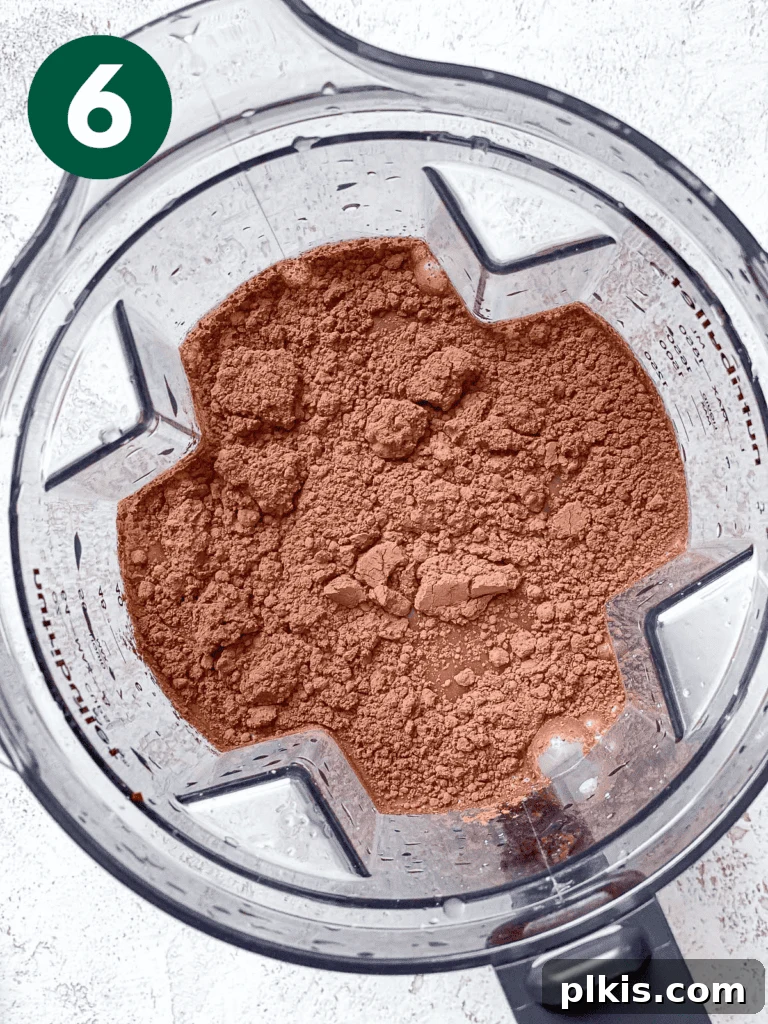 Process shot showing cocoa powder, sweetener, and salt being added to the oat milk in the blender.