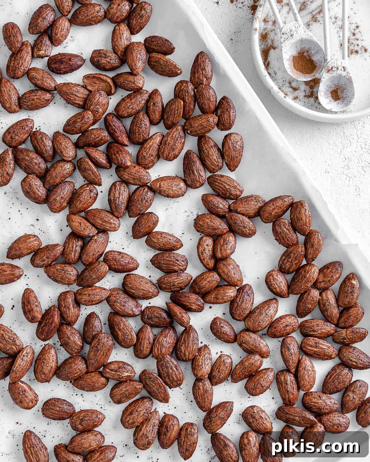 Crispy, golden roasted cinnamon almonds scattered against a pristine white surface, ready to be enjoyed as a wholesome snack or versatile topping.