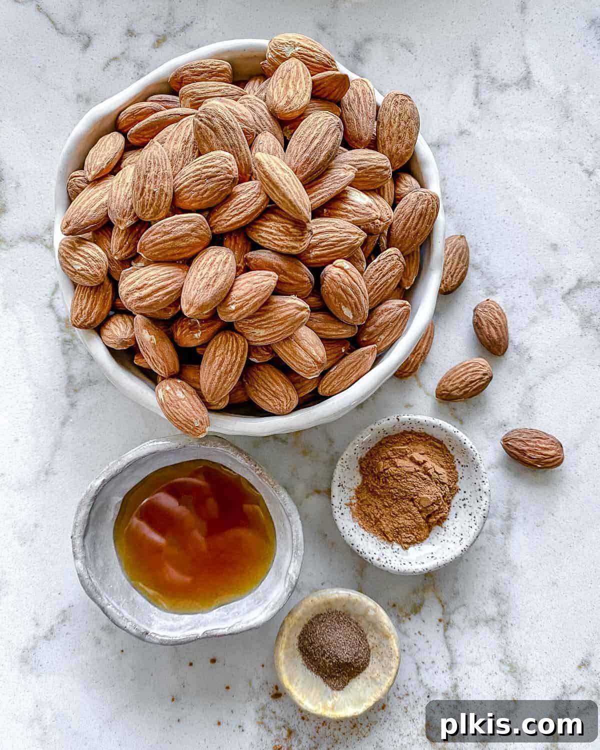 Individually measured ingredients for cinnamon almonds neatly arranged in separate bowls against a elegant white marble surface, ready for preparation.
