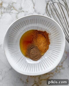 Sweet Heat Cinnamon Almonds 5 Ingredients for cinnamon almonds added to a white bowl against a white surface, ready for mixing.