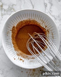 Sweet Heat Cinnamon Almonds 6 The process of mixing spices for cinnamon almonds in a white bowl with a mixer, ensuring thorough blending.