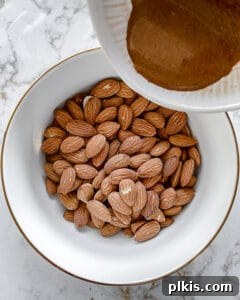 The process showing spices being added to almonds in a white bowl, ensuring an even coating.