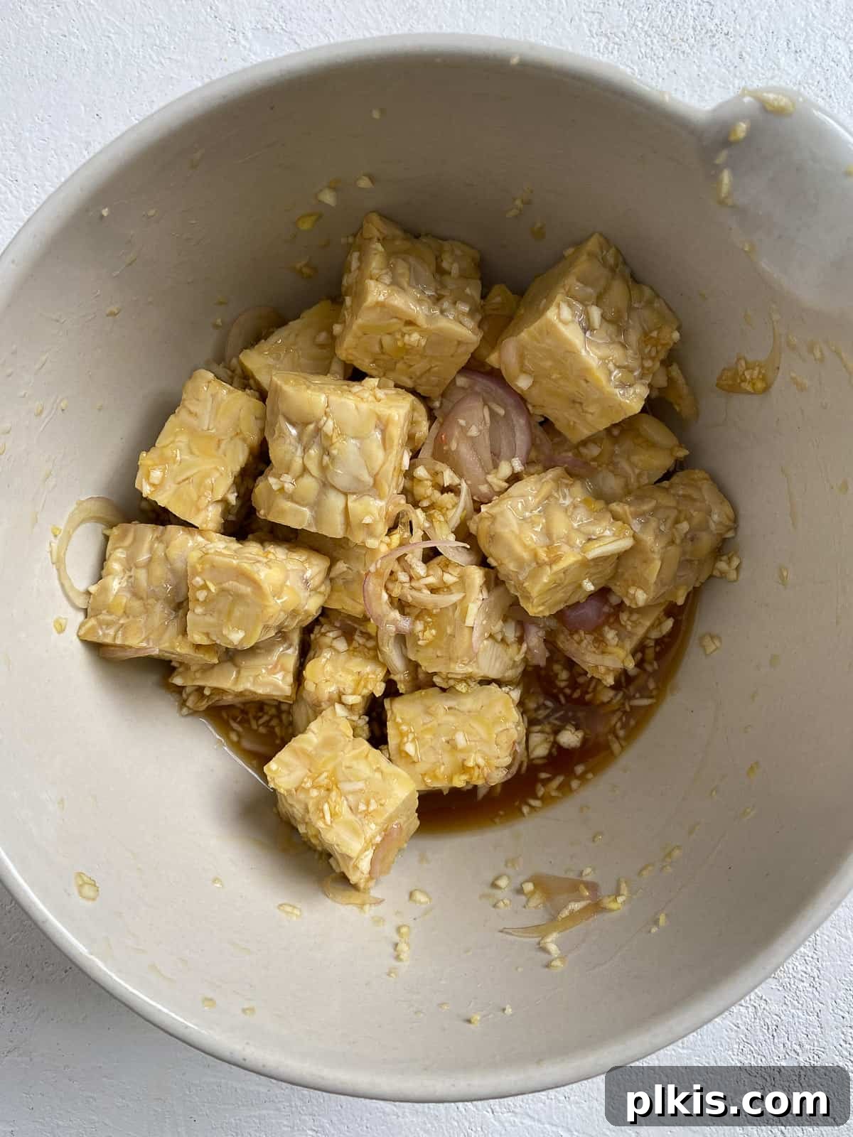 Process shot of mixing cubed tempeh and marinating sauce together in a bowl, ensuring each piece is fully coated.
