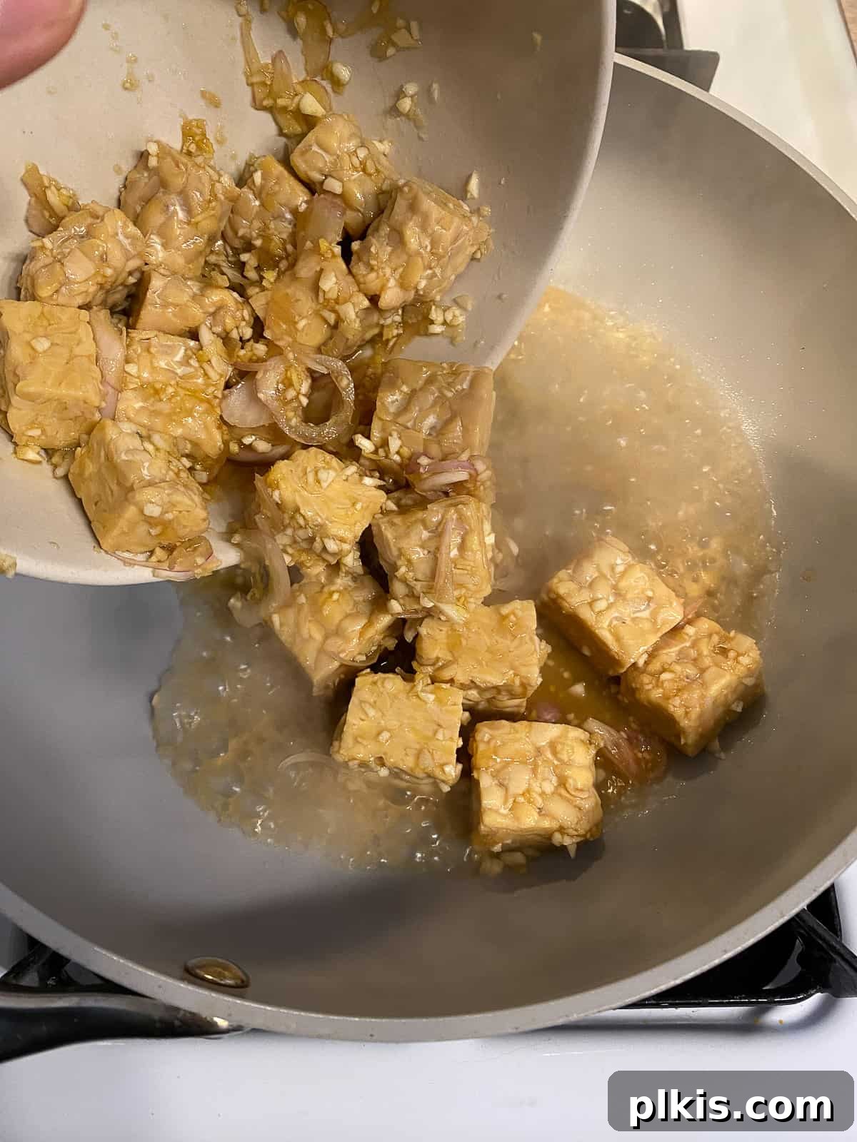 Process shot of adding marinated tempeh to a hot pan to begin searing.