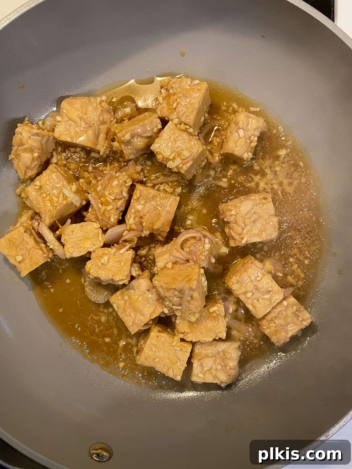 Process shot of marinated tempeh sizzling in a pan, beginning to develop a sear.