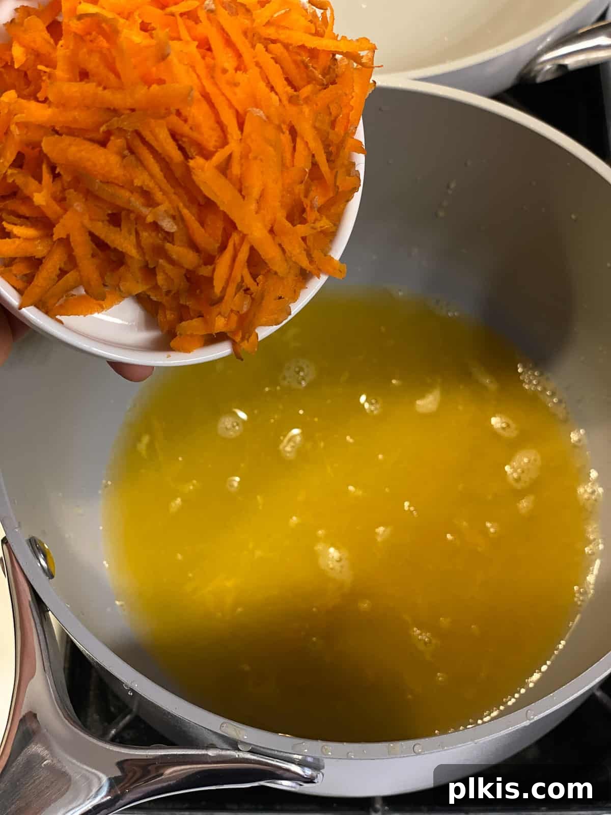 Process shot of adding grated carrots to a pot with other glaze ingredients.