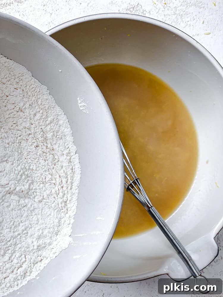 Zesty Lemon Poppy Seed Cake 5 Process shot showing dry ingredients being added to the wet mixture in a bowl.