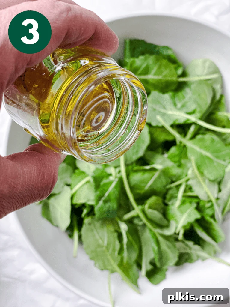 Power-Packed Kale Quinoa Salad 6 A process shot demonstrating olive oil being drizzled over fresh greens in a bowl, preparing for the kale massage step.