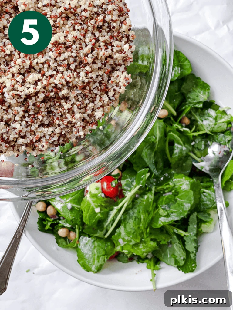 Power-Packed Kale Quinoa Salad 8 A process shot illustrating cooked quinoa being added to a bowl filled with vibrant greens and other salad components.