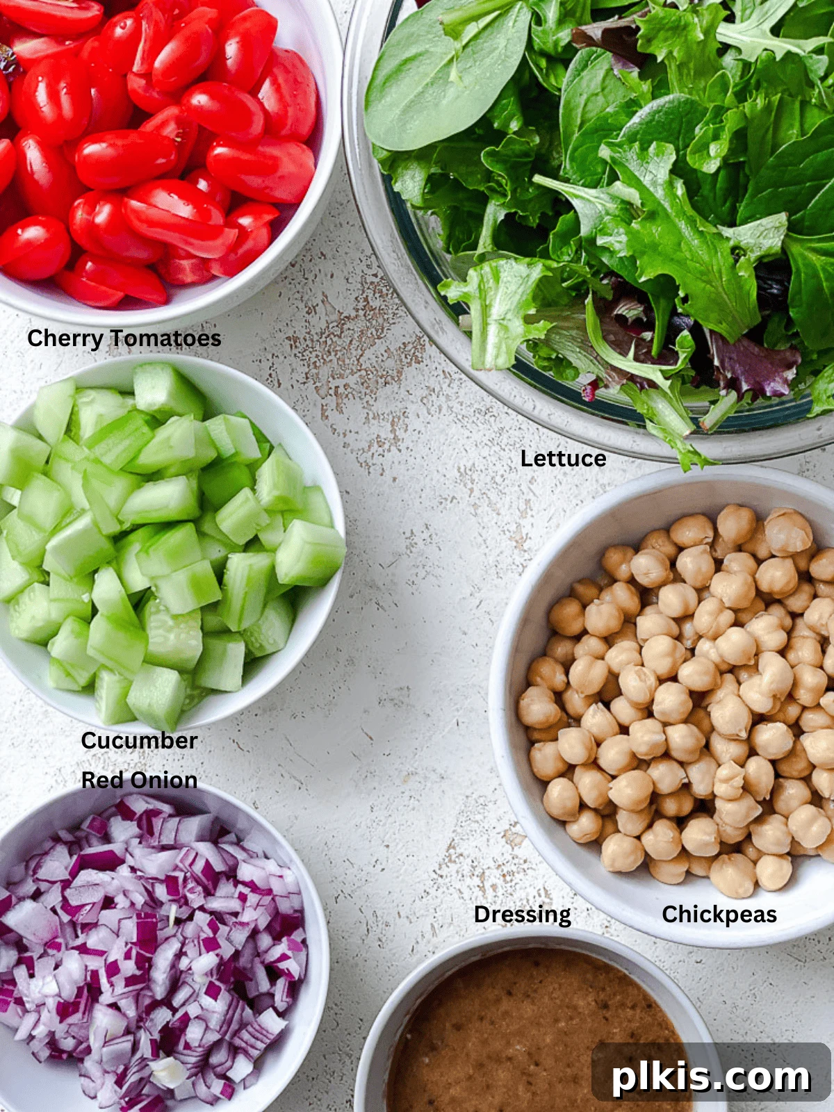 Jarred Quinoa Chickpea Power Salad 3 A collection of fresh ingredients for Quinoa Chickpea Salad, including chickpeas, quinoa, lettuce, cherry tomatoes, cucumber, red onion, and pumpkin seeds, neatly arranged on a white surface.