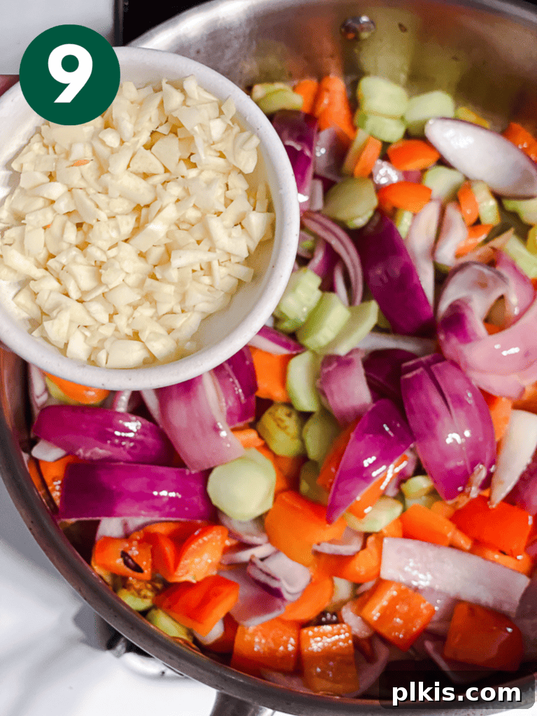 Process shot of adding minced garlic to the cooking vegetables in the pan.