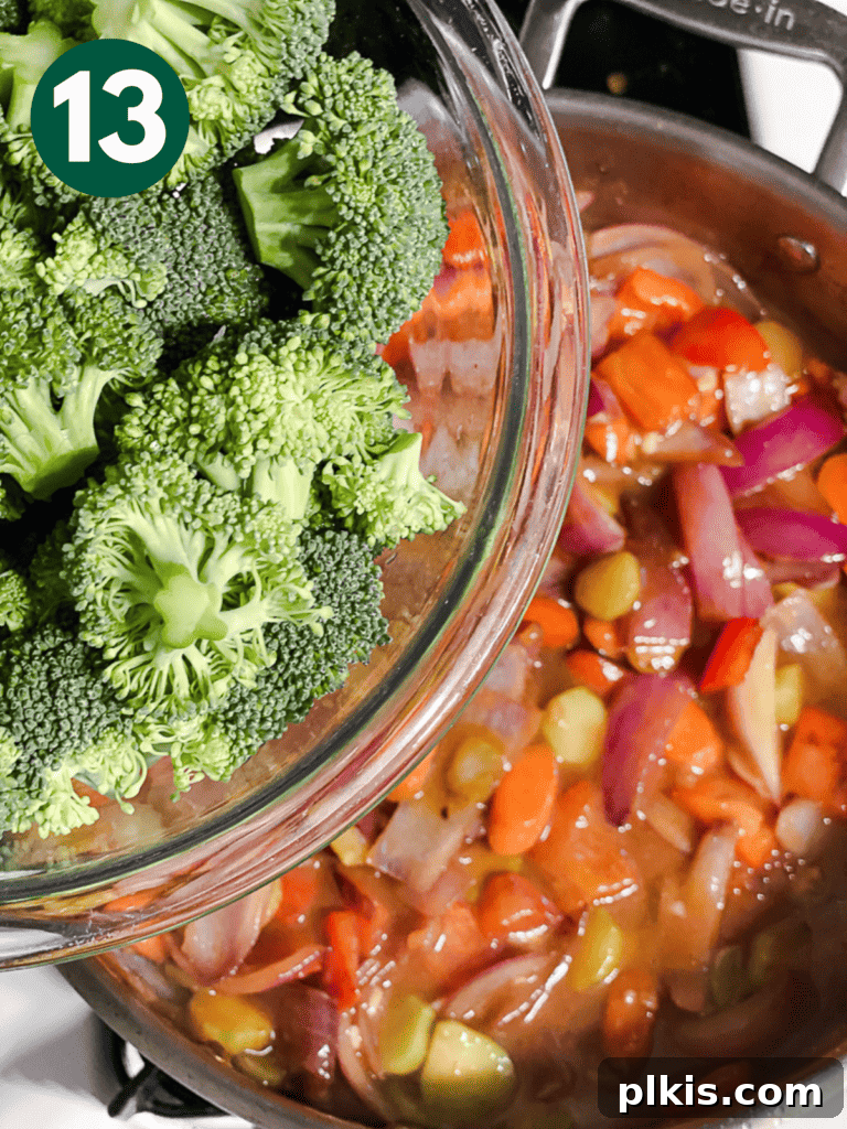 Process shot of adding fresh broccoli florets to the sauced vegetables in the pan.