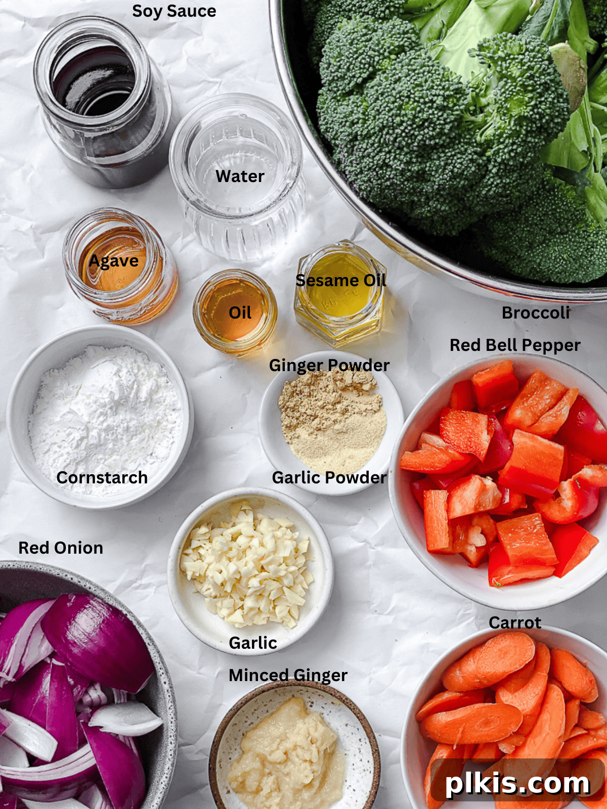 Various ingredients for Easy Garlic Broccoli Stir-Fry laid out on a white surface, including broccoli, carrots, bell peppers, onion, garlic, ginger, soy sauce, and spices.