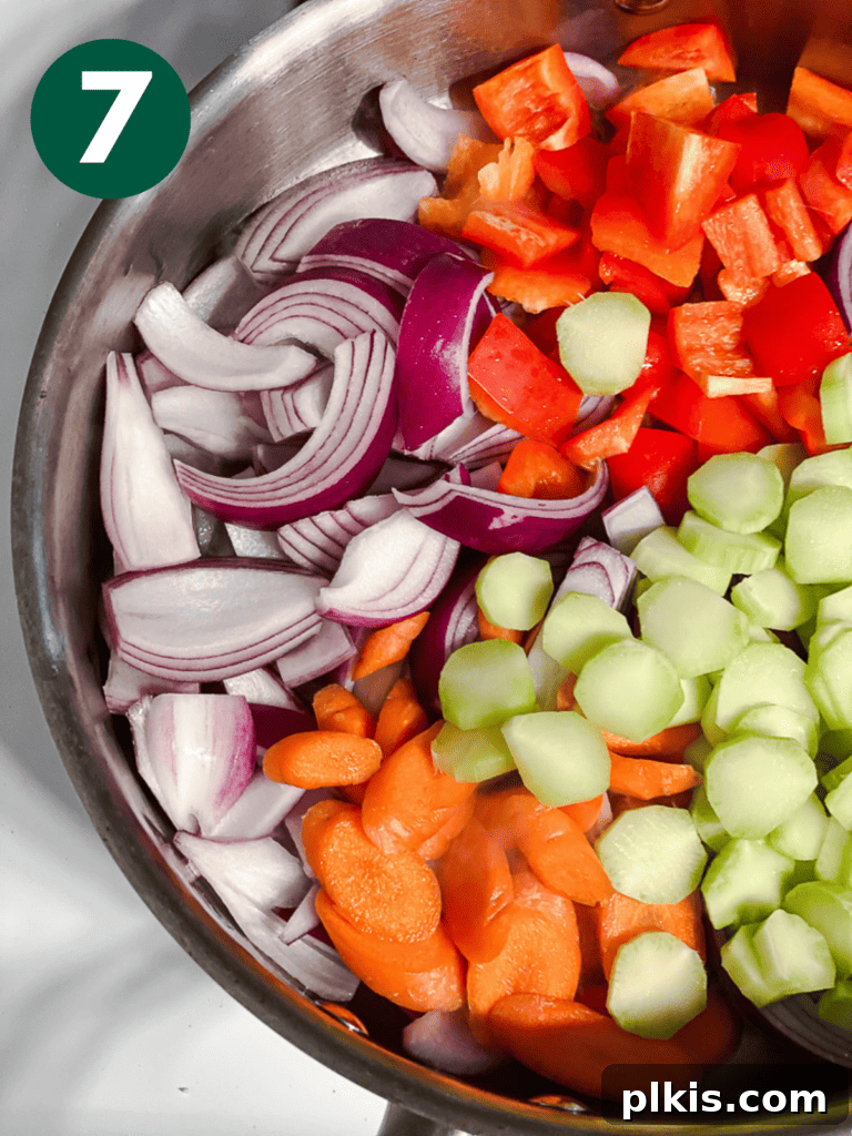 Process shot showing mixed vegetables (onion, bell pepper, carrot, broccoli stems) cooking in a hot pan.