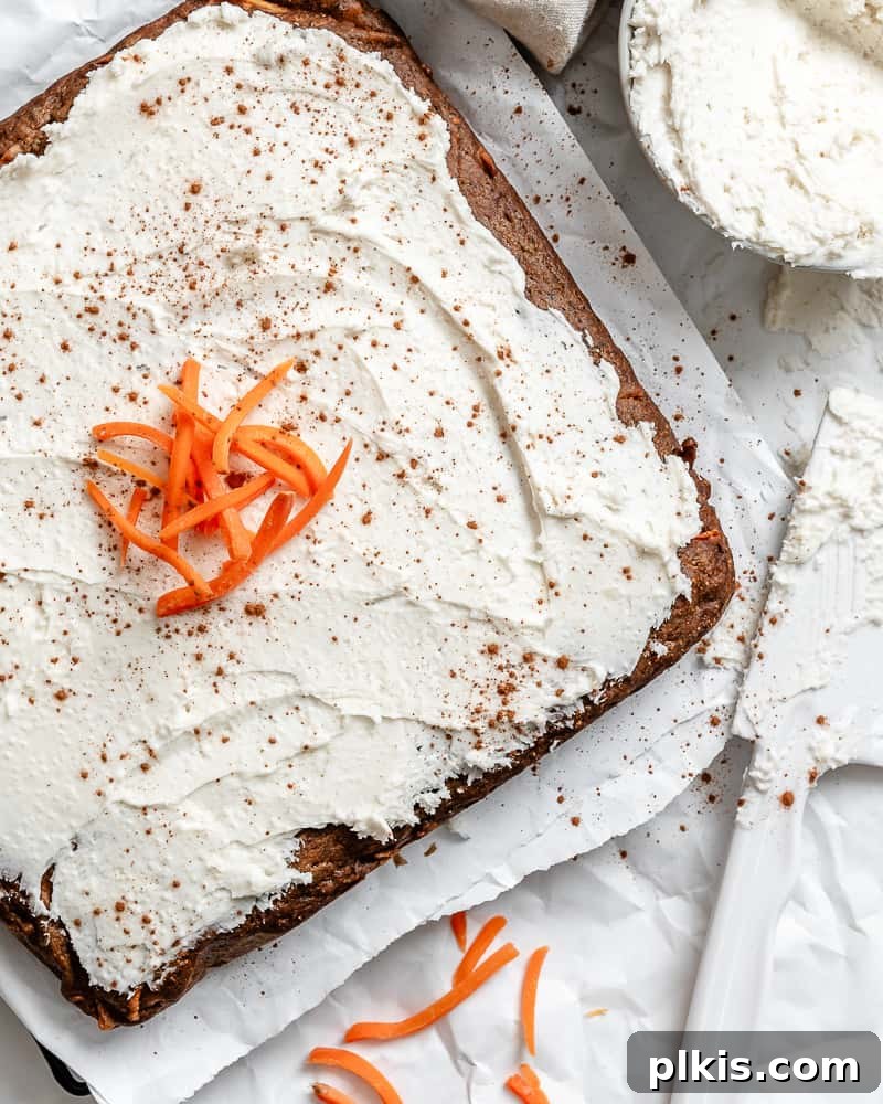 A perfectly baked and frosted Vegan Carrot Cake on a clean white surface, garnished with chopped walnuts and fresh carrot curls.