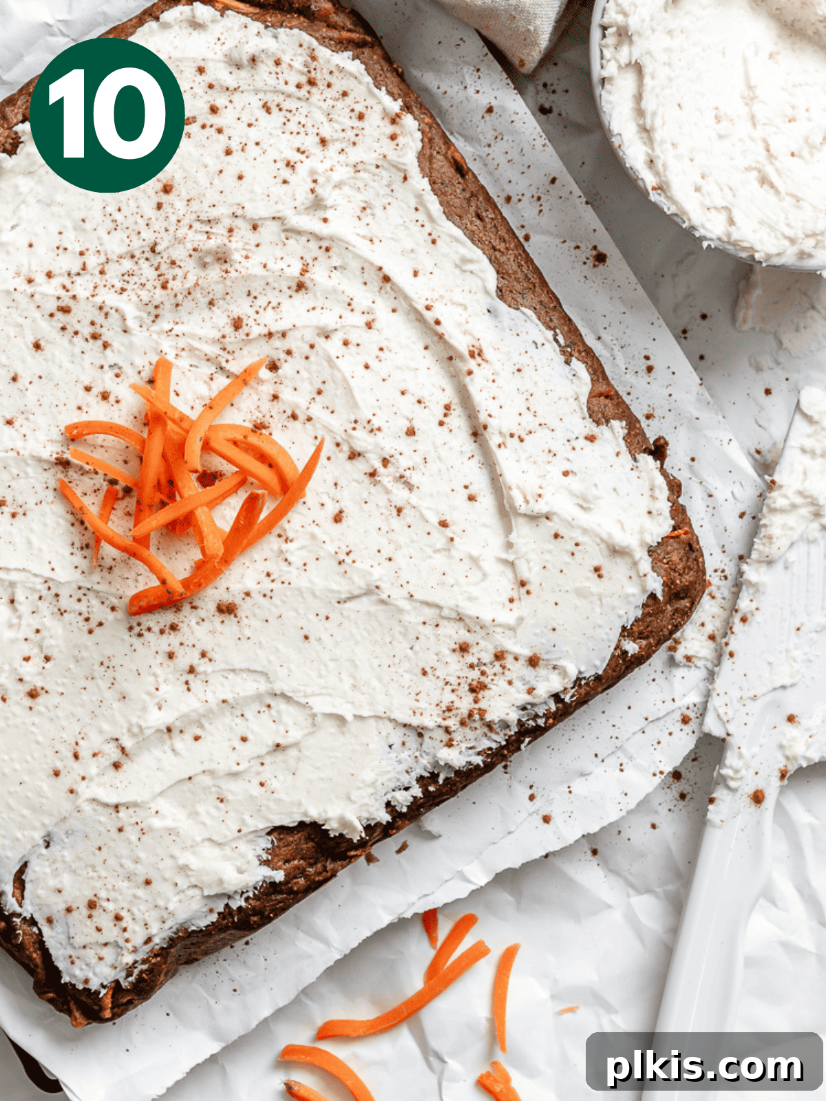A beautifully frosted Vegan Carrot Cake, adorned with decorative swirls of frosting and perhaps a sprinkle of cinnamon, resting on a cooling rack.