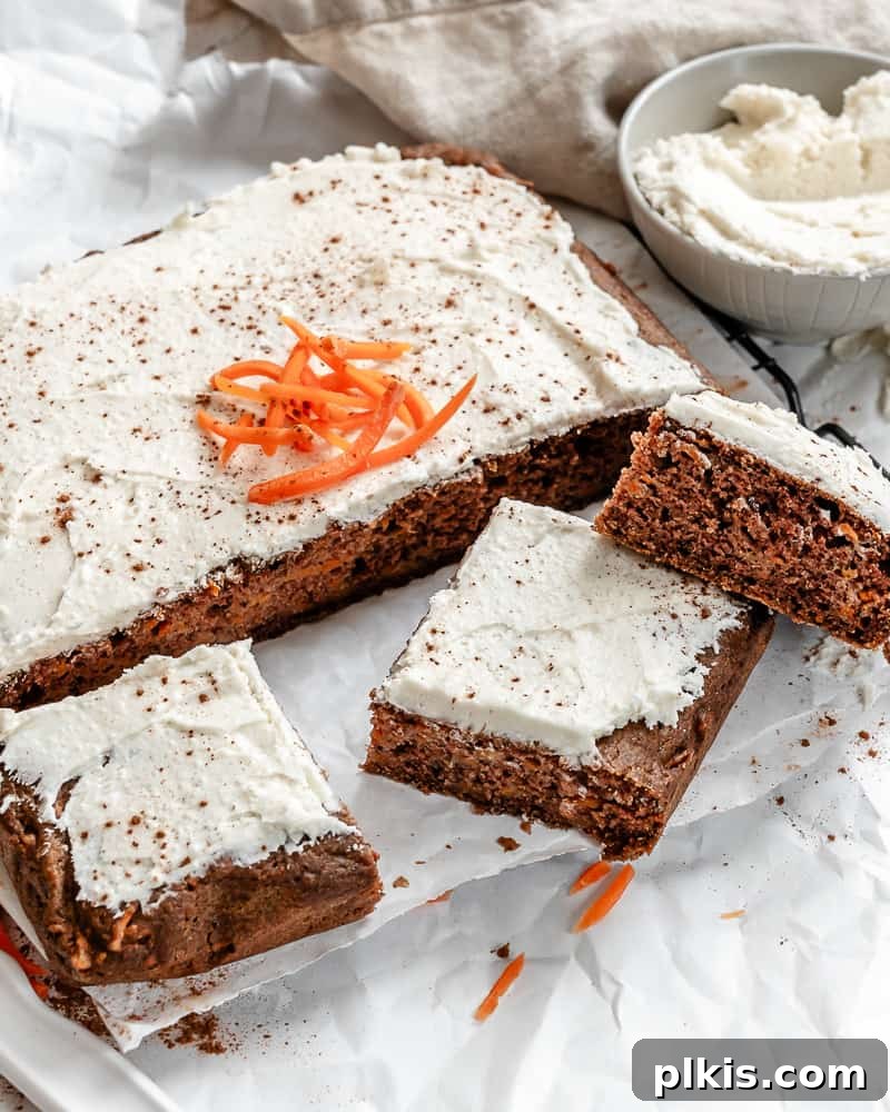 A close-up shot of a slice of Vegan Carrot Cake, revealing its moist crumb, bits of carrot, and walnuts, with a generous layer of frosting.