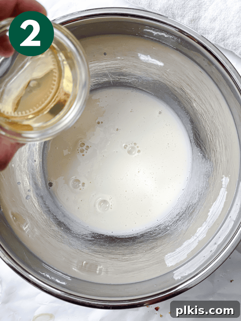 A process shot showing apple cider vinegar being added to a bowl of plant-based milk, initiating the vegan buttermilk reaction.