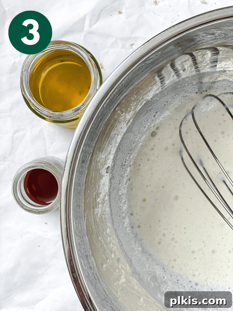 A close-up process shot of wet ingredients, including plant milk, vinegar, vanilla, and oil, being mixed together in a bowl.