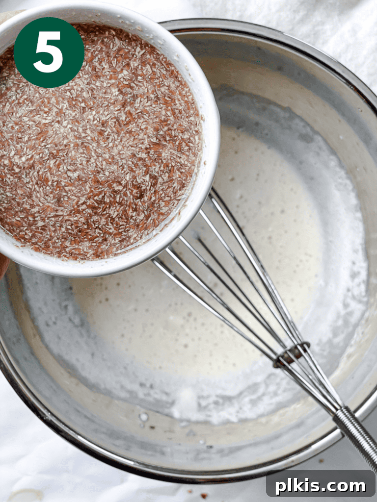 A process shot demonstrating the addition of the flaxseed mixture to the dry ingredients in a large mixing bowl.