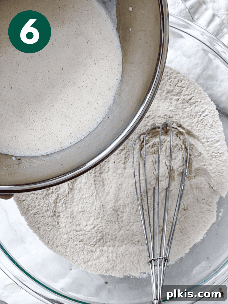 A process shot illustrating the wet liquid mixture being poured into the dry ingredients in a mixing bowl.
