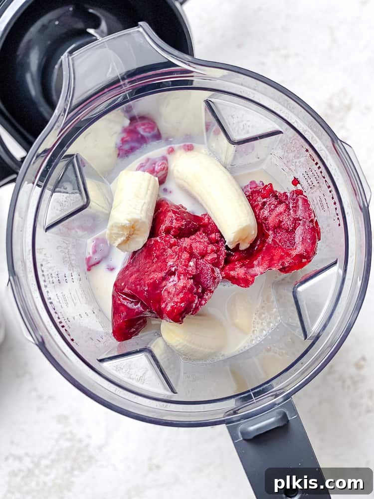 Effortless Raspberry Refresh 4 Process shot showing all the main ingredients for a raspberry smoothie being added into a blender cup.