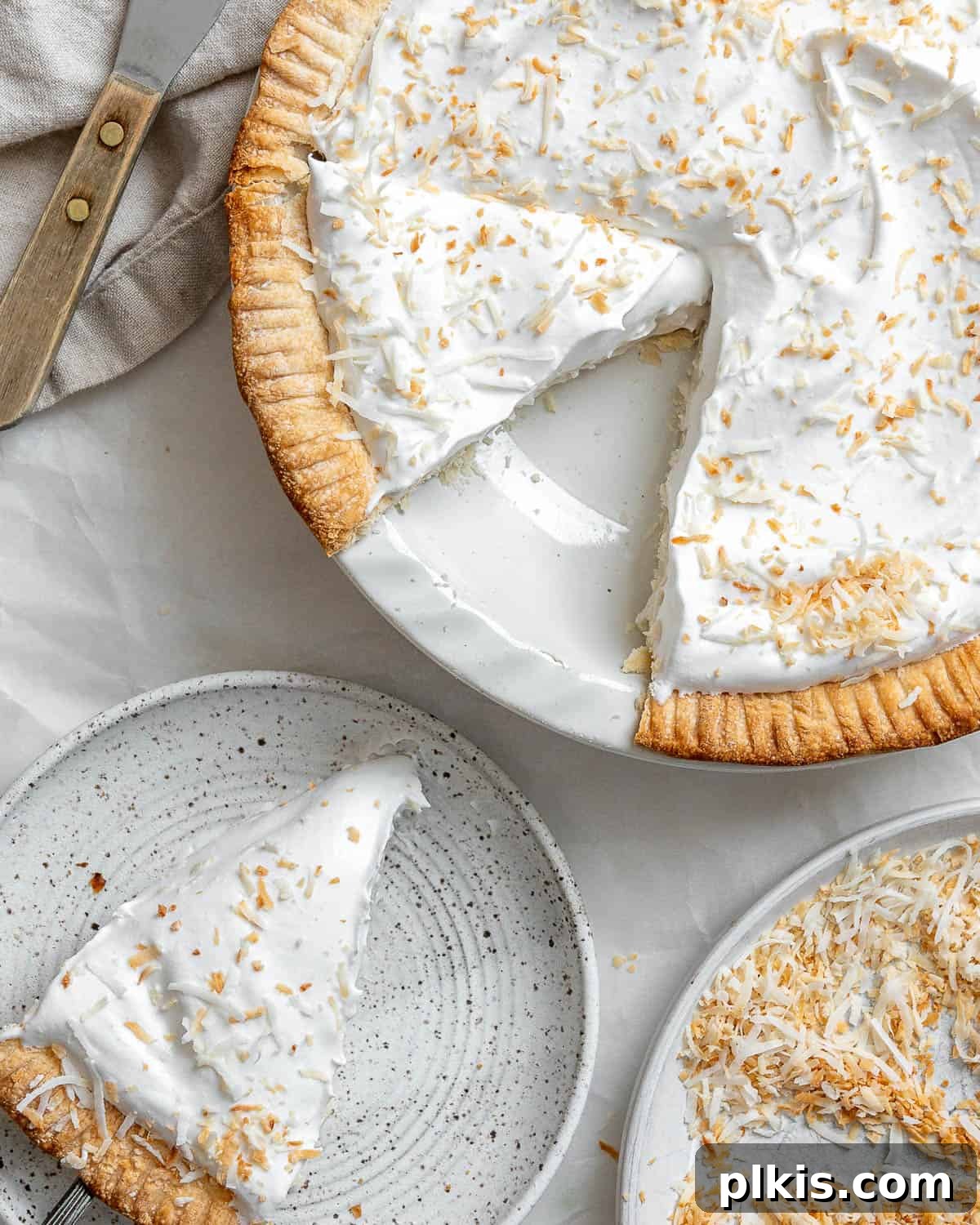 Velvety Vegan Coconut Dream Pie 9 A whole Vegan Coconut Cream Pie beautifully decorated with whipped cream and toasted coconut, set against a pristine white background, showcasing its festive appeal.