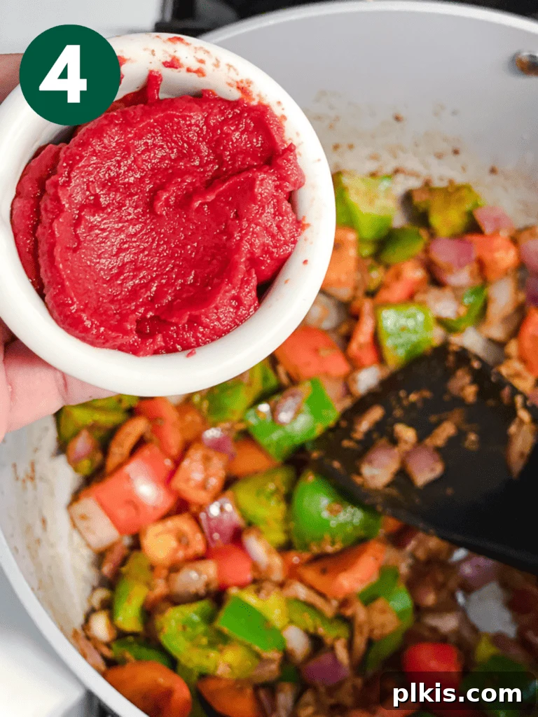 Hearty Lentil and Bean Chili 7 Tomato paste being added to the spiced vegetables in the pot, creating a vibrant, rich foundation for the chili.