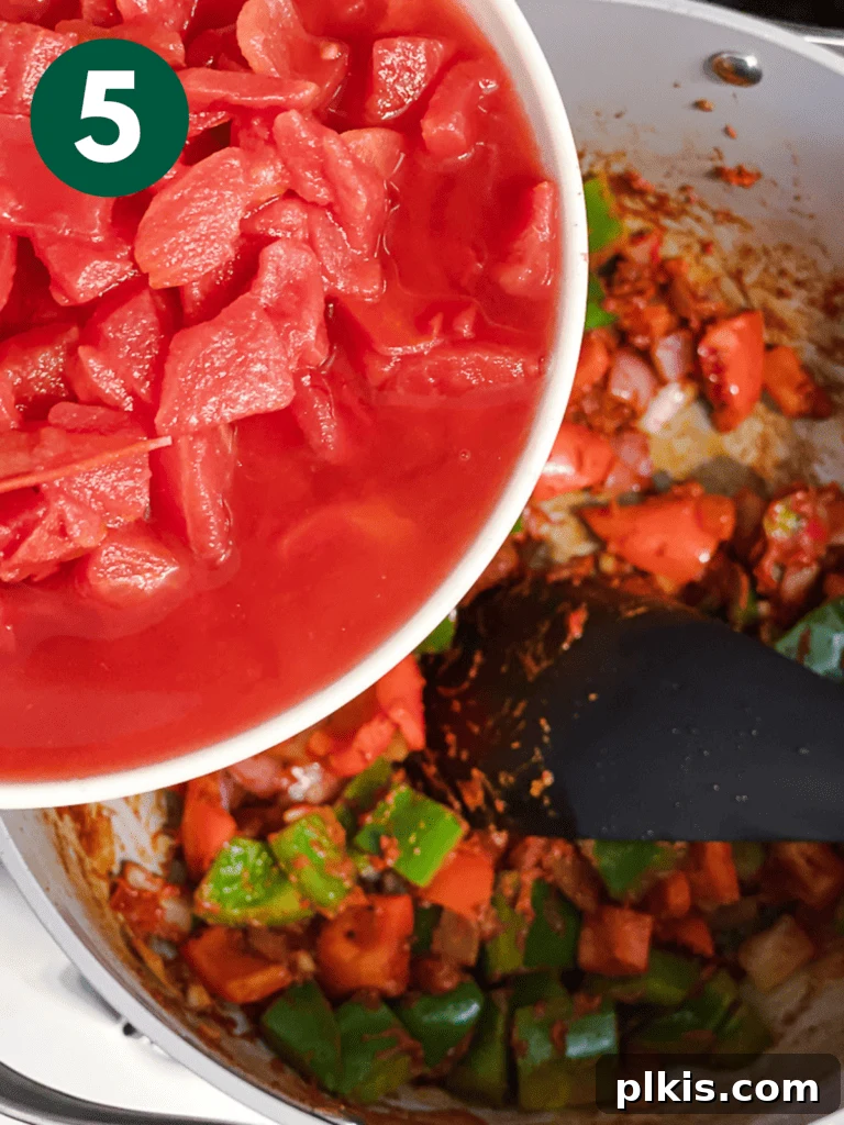 Hearty Lentil and Bean Chili 8 Canned diced tomatoes being poured into the pot, mixing with the cooked aromatics and spices.