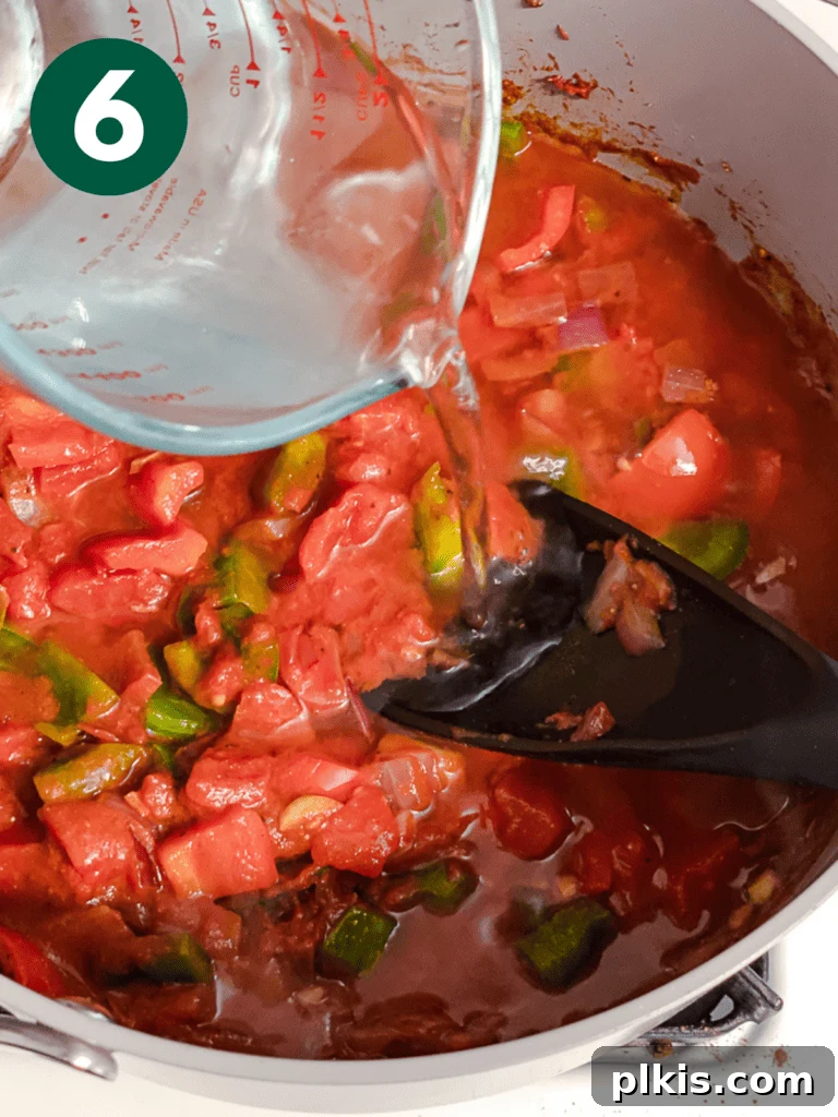Hearty Lentil and Bean Chili 9 Water or broth being added to the chili mixture in the pot, providing the liquid base for simmering.