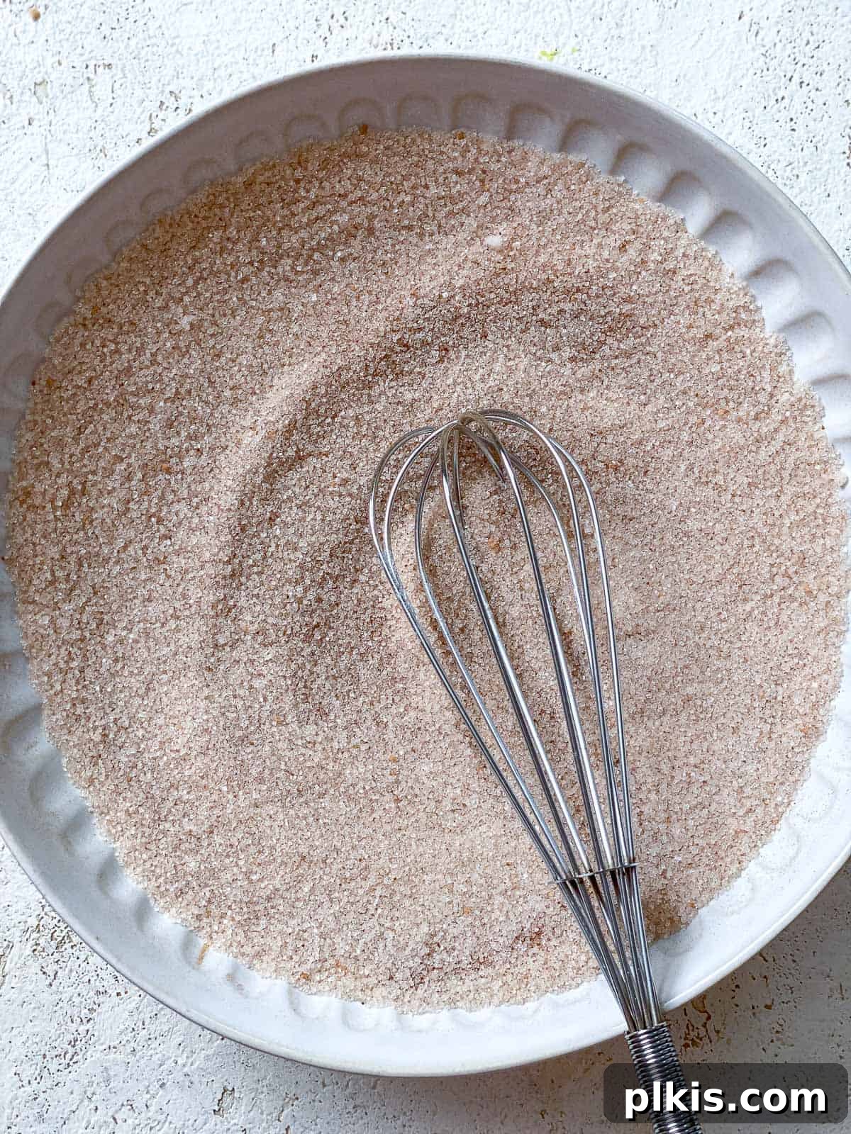 Vegan Churro Bliss 11 A whisk blending cinnamon and granulated sugar in a white bowl, creating the churro coating mixture.