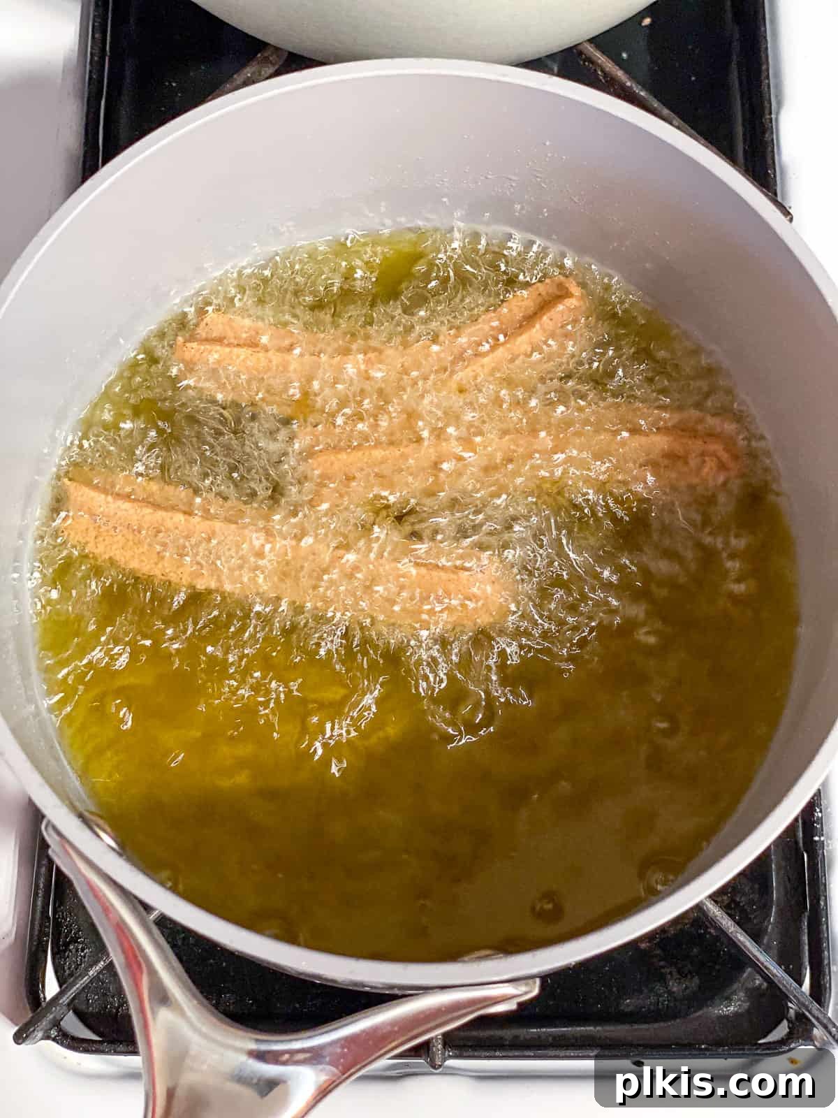 Vegan Churro Bliss 14 Three vegan churros deep-frying in hot oil in a saucepan, turning golden brown.