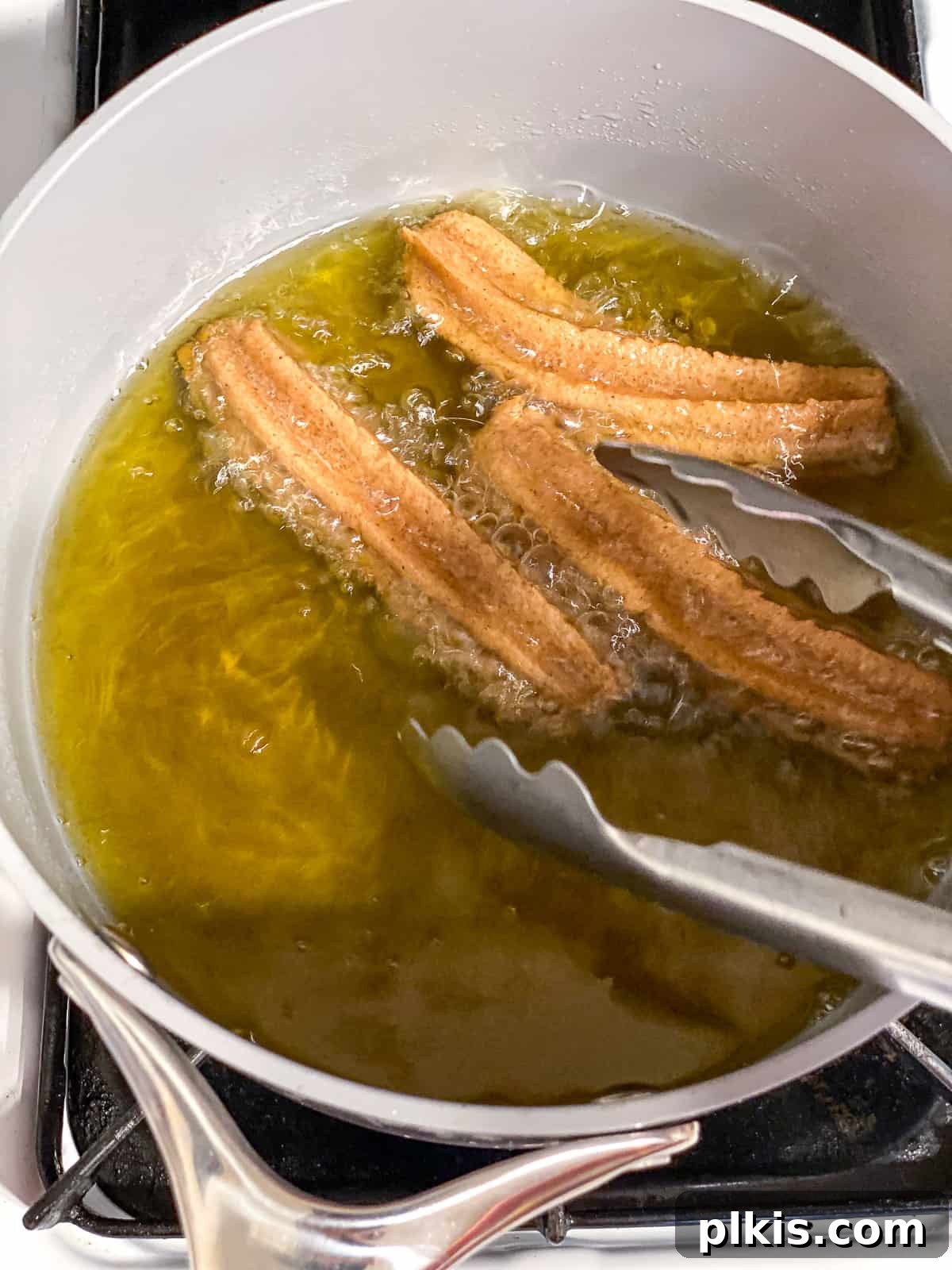 Vegan Churro Bliss 15 Using metal tongs to carefully remove three fried vegan churros from a saucepan of hot oil.